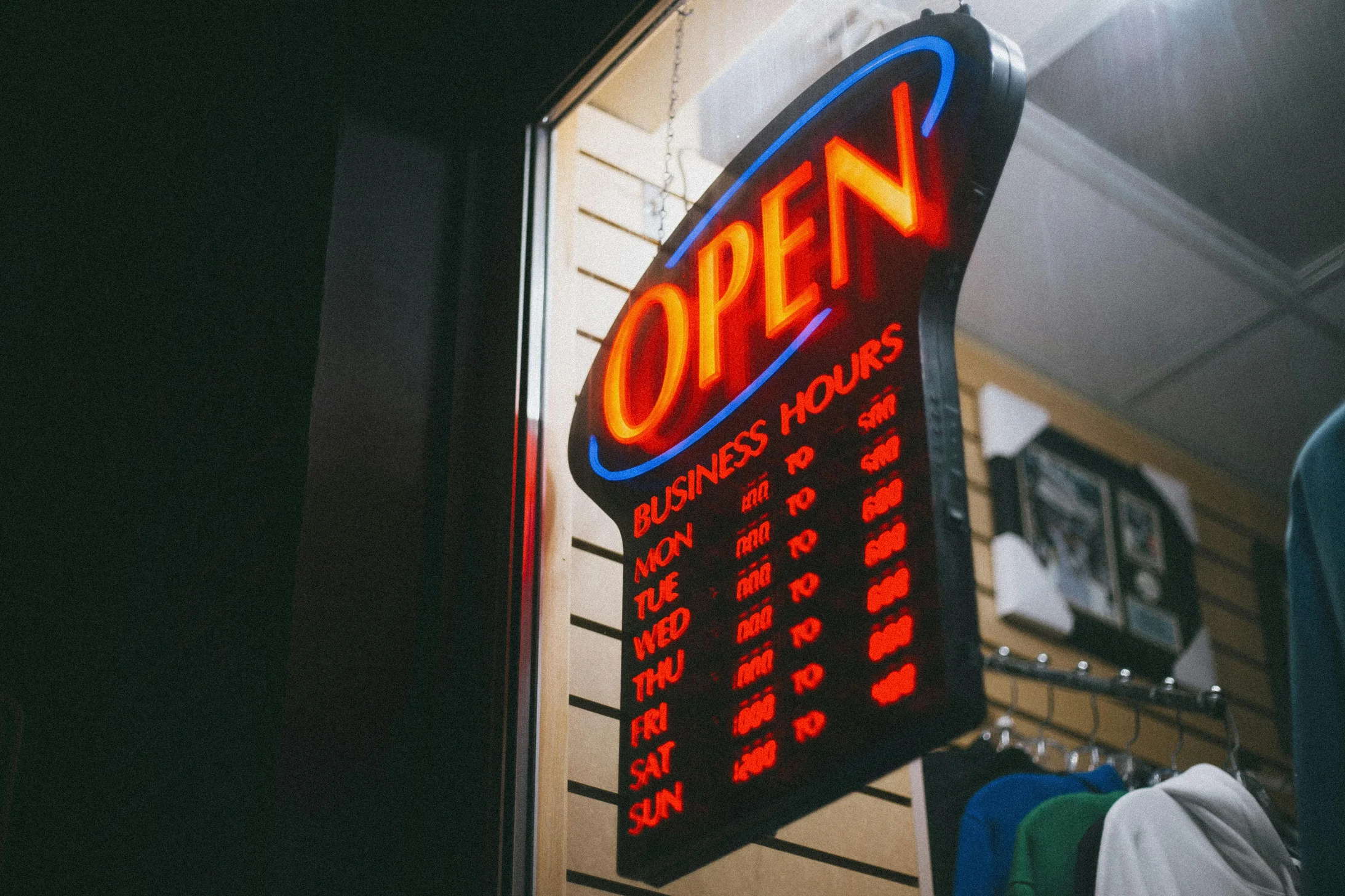 Vibrant neon 'Open' sign displaying business hours inside a shop at night.