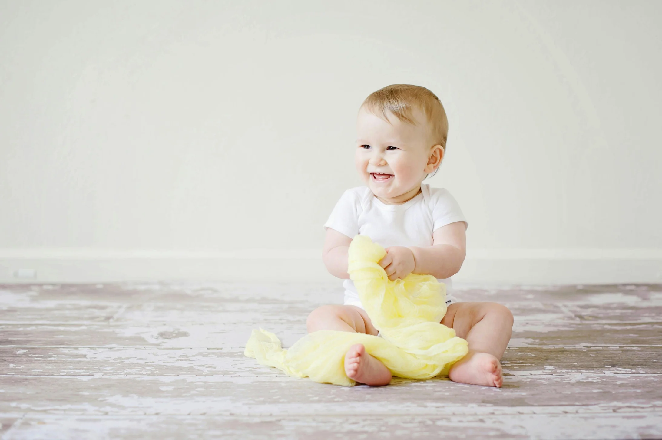 Adorable baby laughing while sitting on the floor with a yellow blanket indoors, showcasing happiness and innocence.