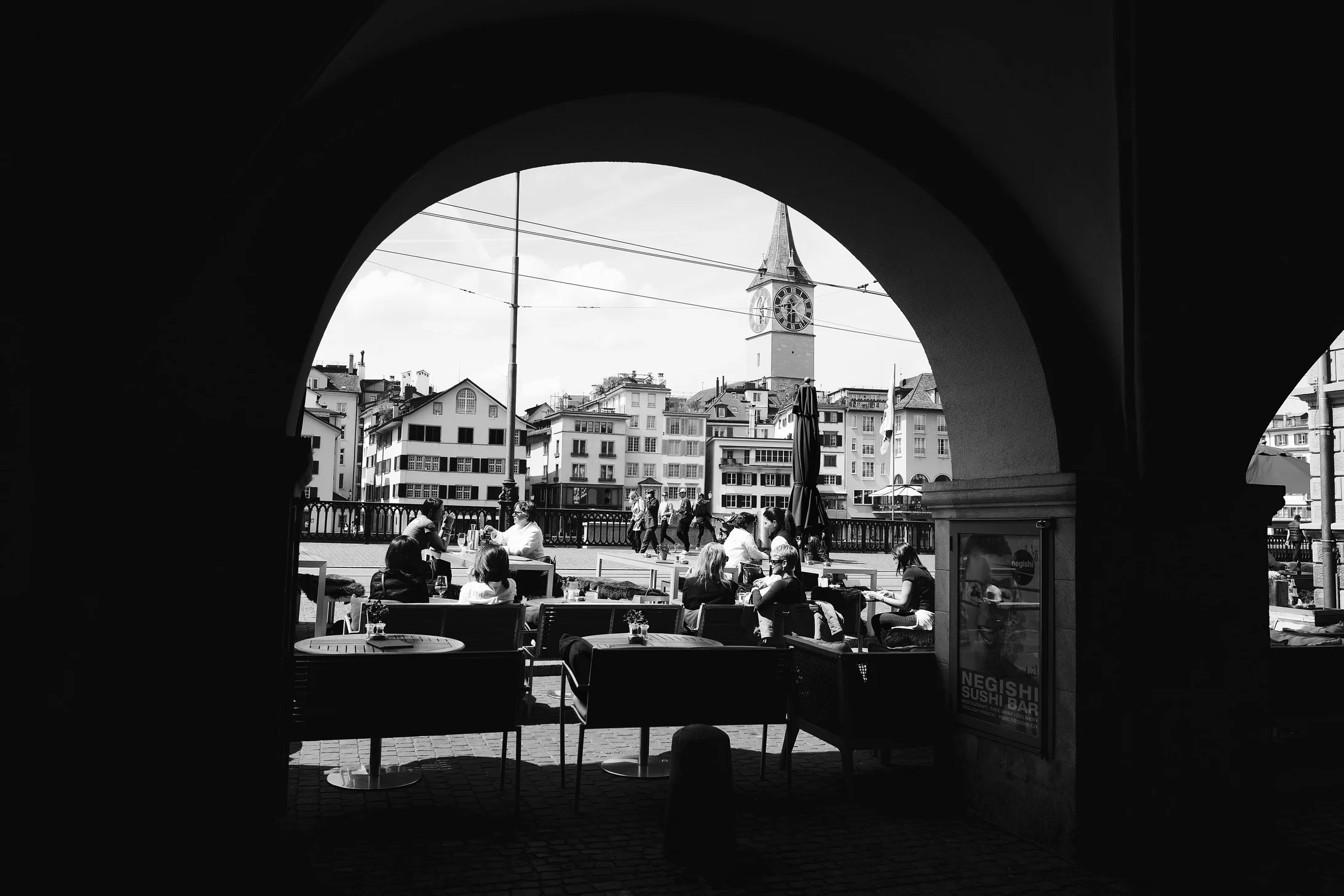 Arched view of Zurich with people dining, highlighting historic architecture.
