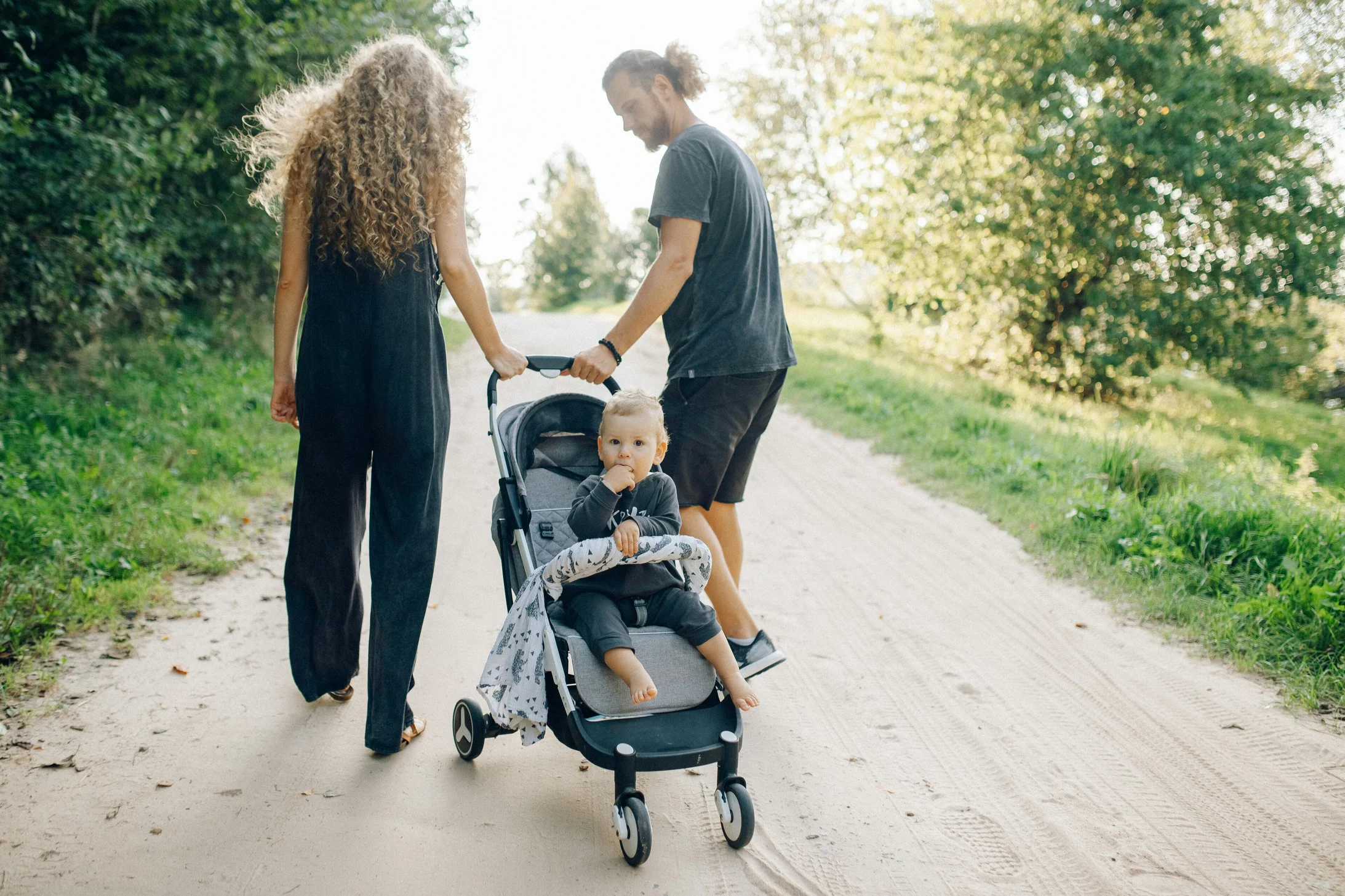 A family walking in a park with a toddler in a stroller on a sunny day.