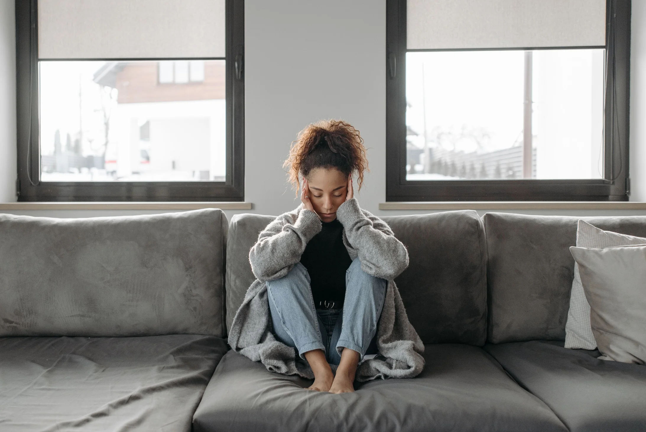 A woman sits on a sofa looking unwell, emphasizing a sense of illness or fatigue indoors.