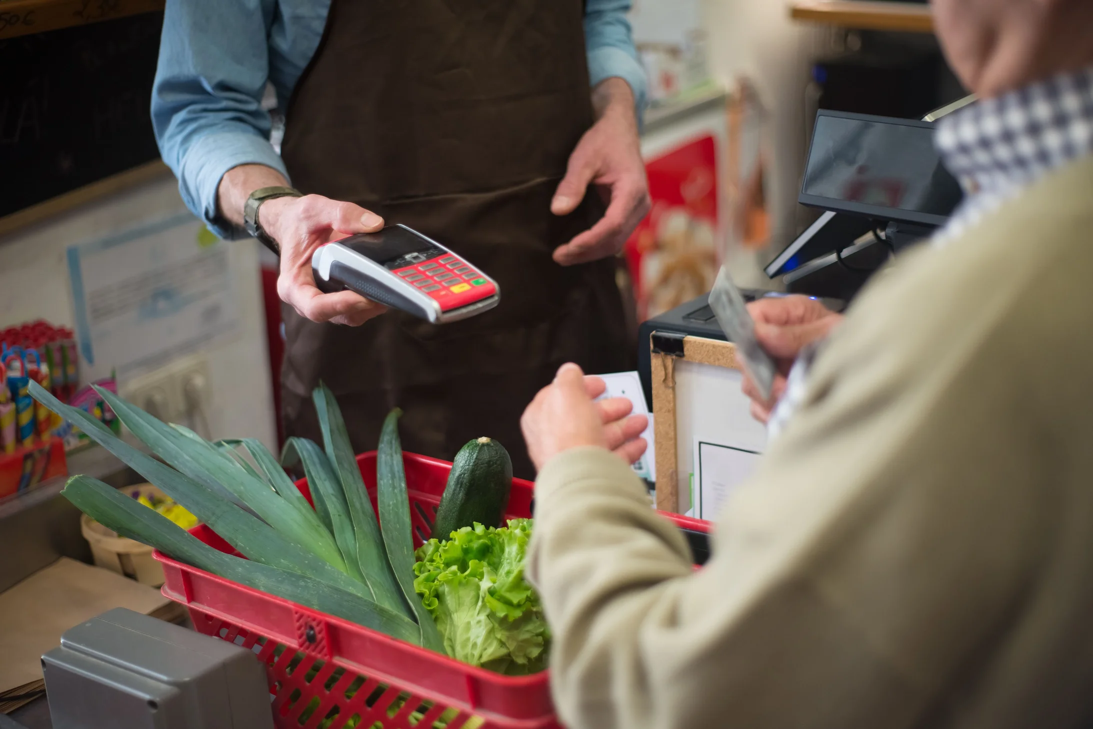 Close-up of customer paying for groceries with produce at a store checkout counter.