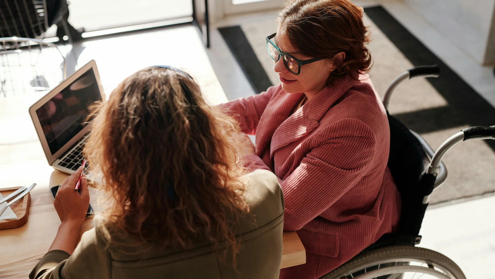 Woman in red sweater wearing black framed eyeglasses sitting on wheelchair
