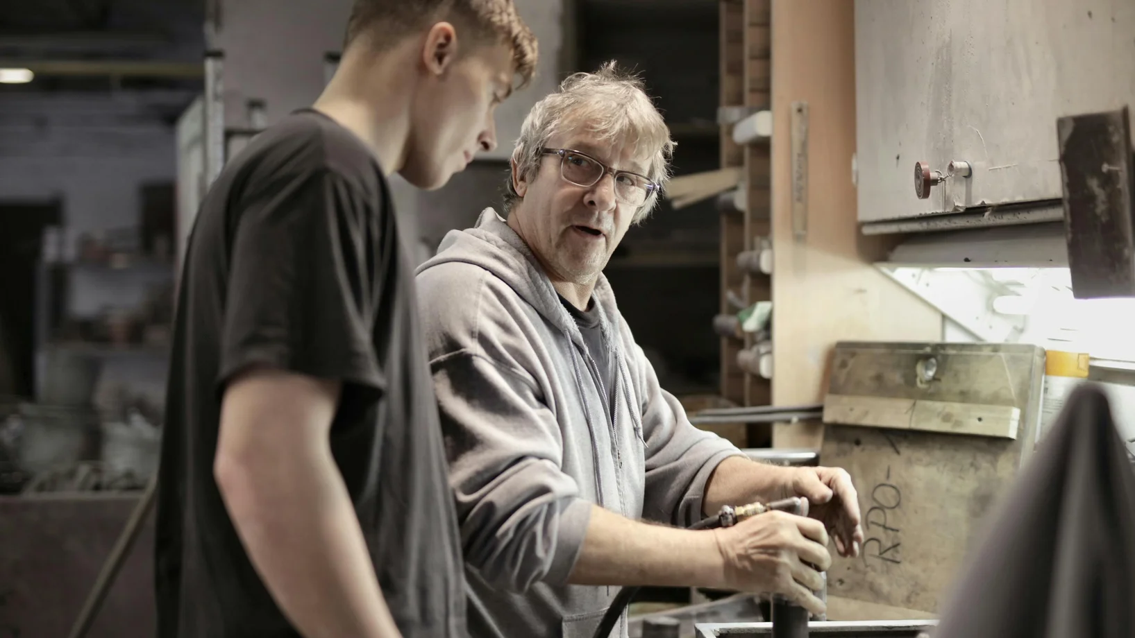Workers handling detail by pneumatic tool in workshop