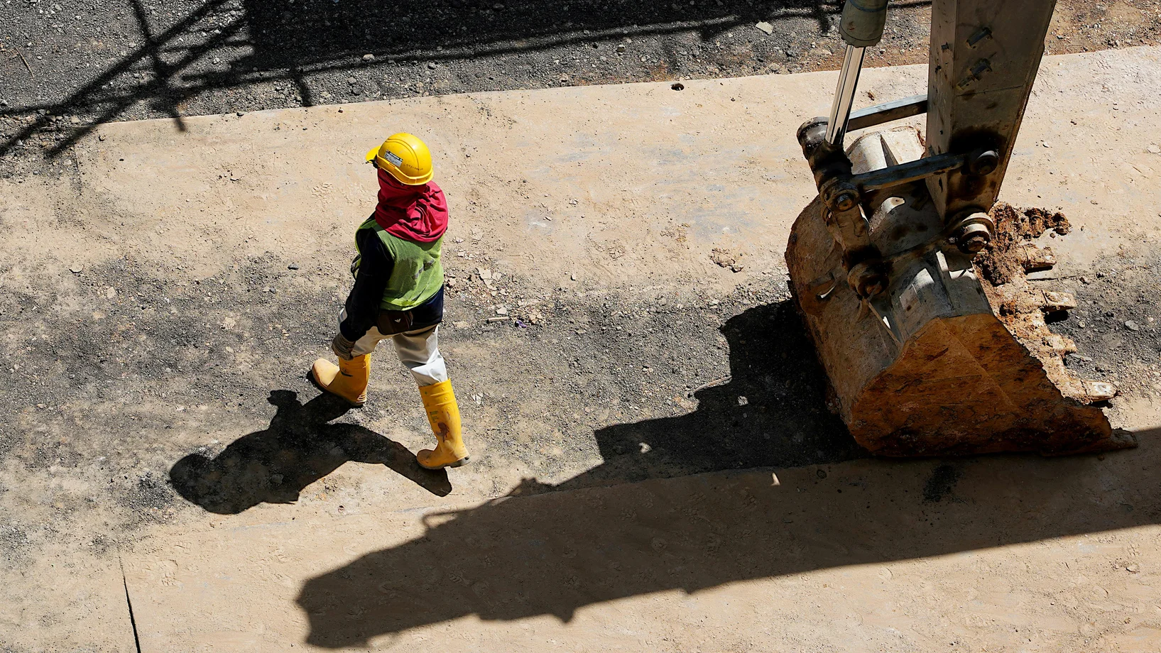 Overhead view of a construction worker walking beside a large excavator.