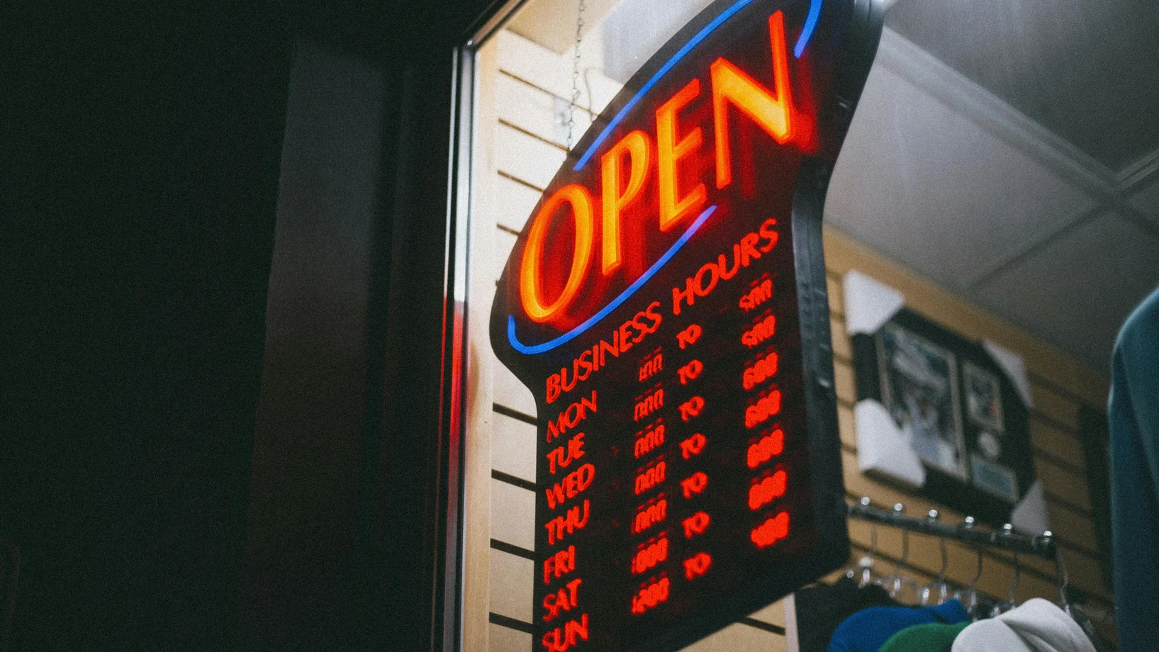 Vibrant neon 'Open' sign displaying business hours inside a shop at night.