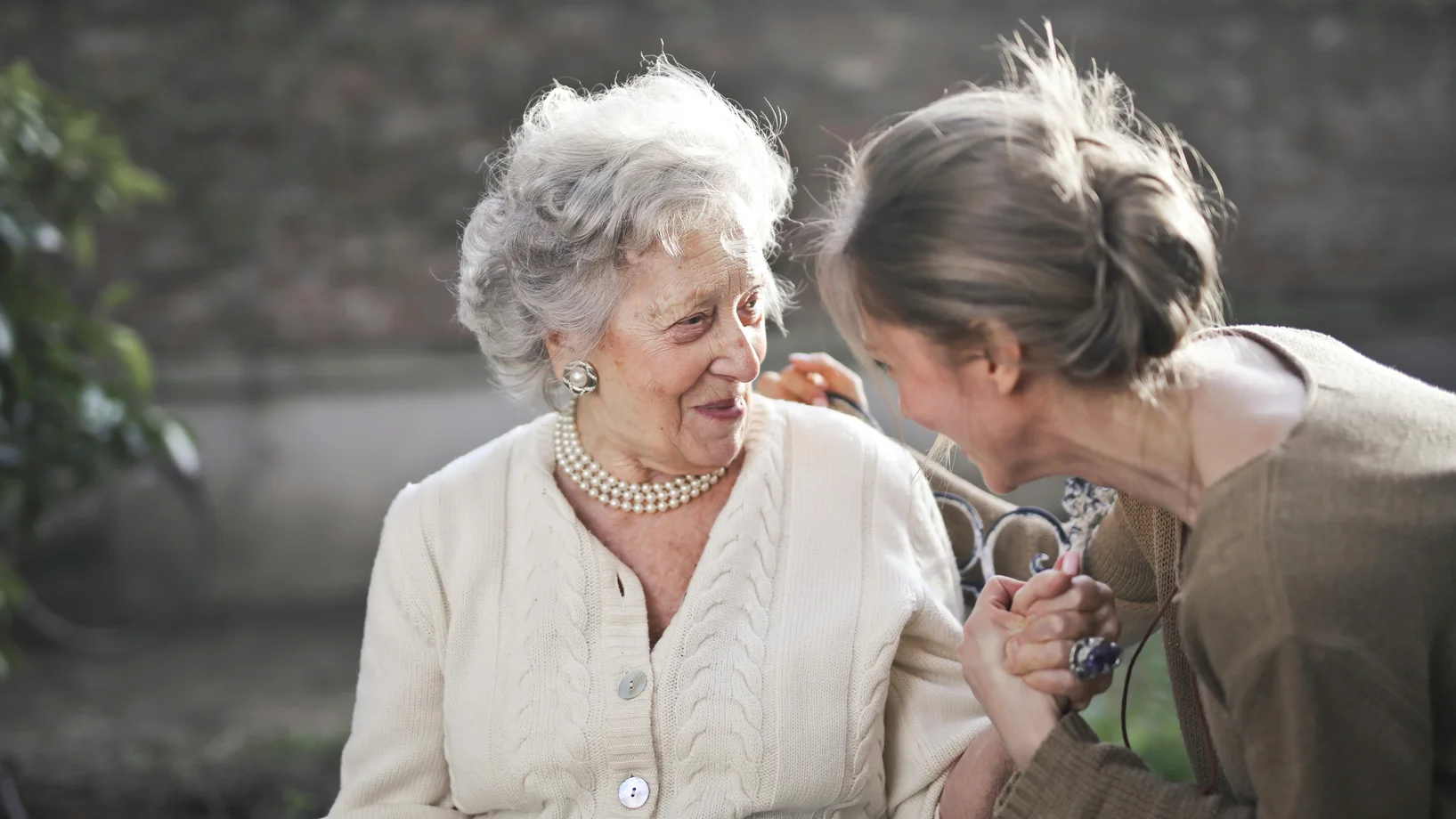 Joyful interaction between an elderly woman and her granddaughter in a sunny outdoor setting.