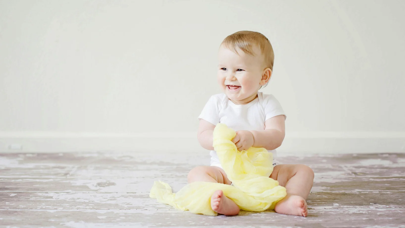 Adorable baby laughing while sitting on the floor with a yellow blanket indoors, showcasing happiness and innocence.