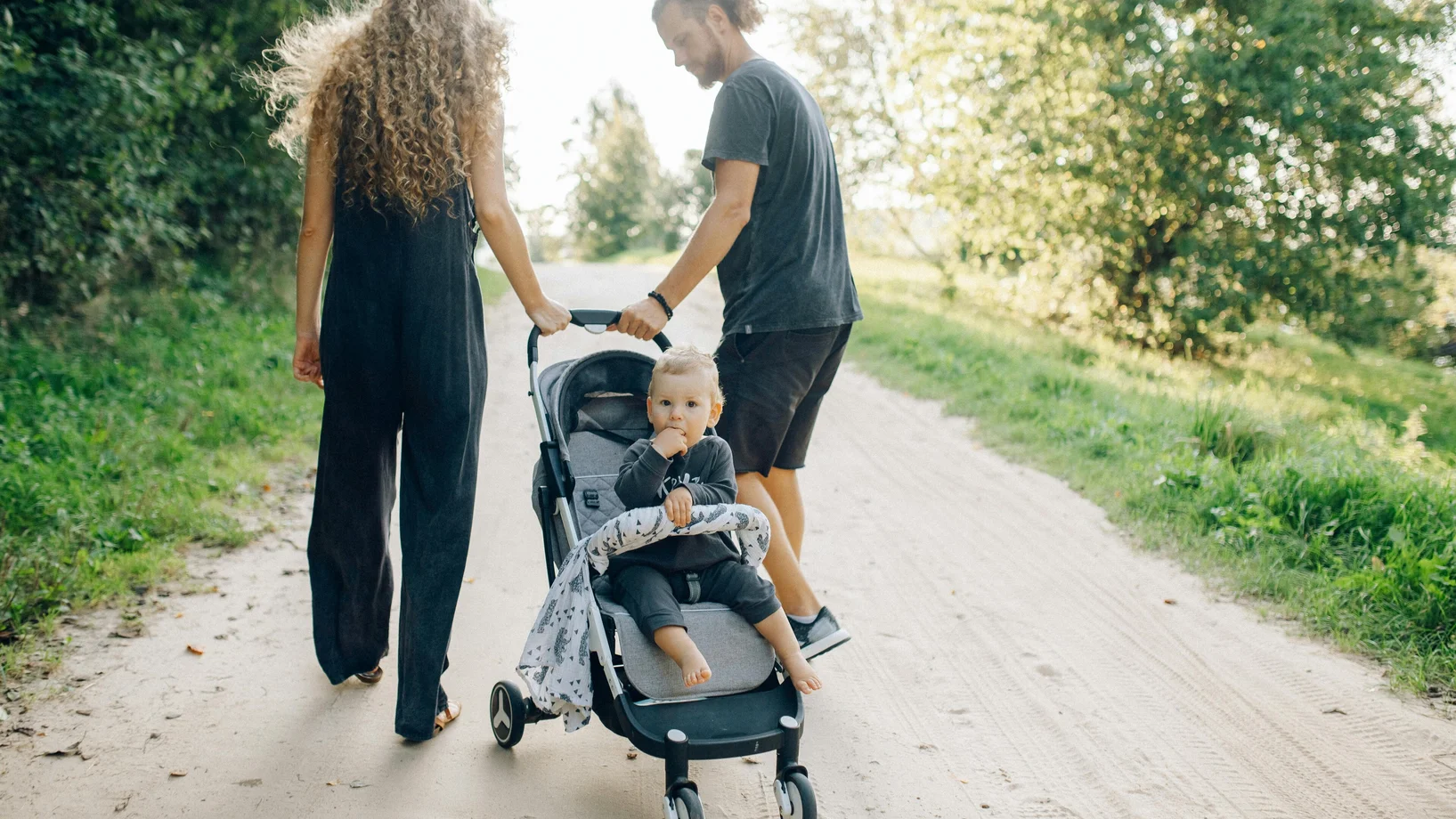 A family walking in a park with a toddler in a stroller on a sunny day.