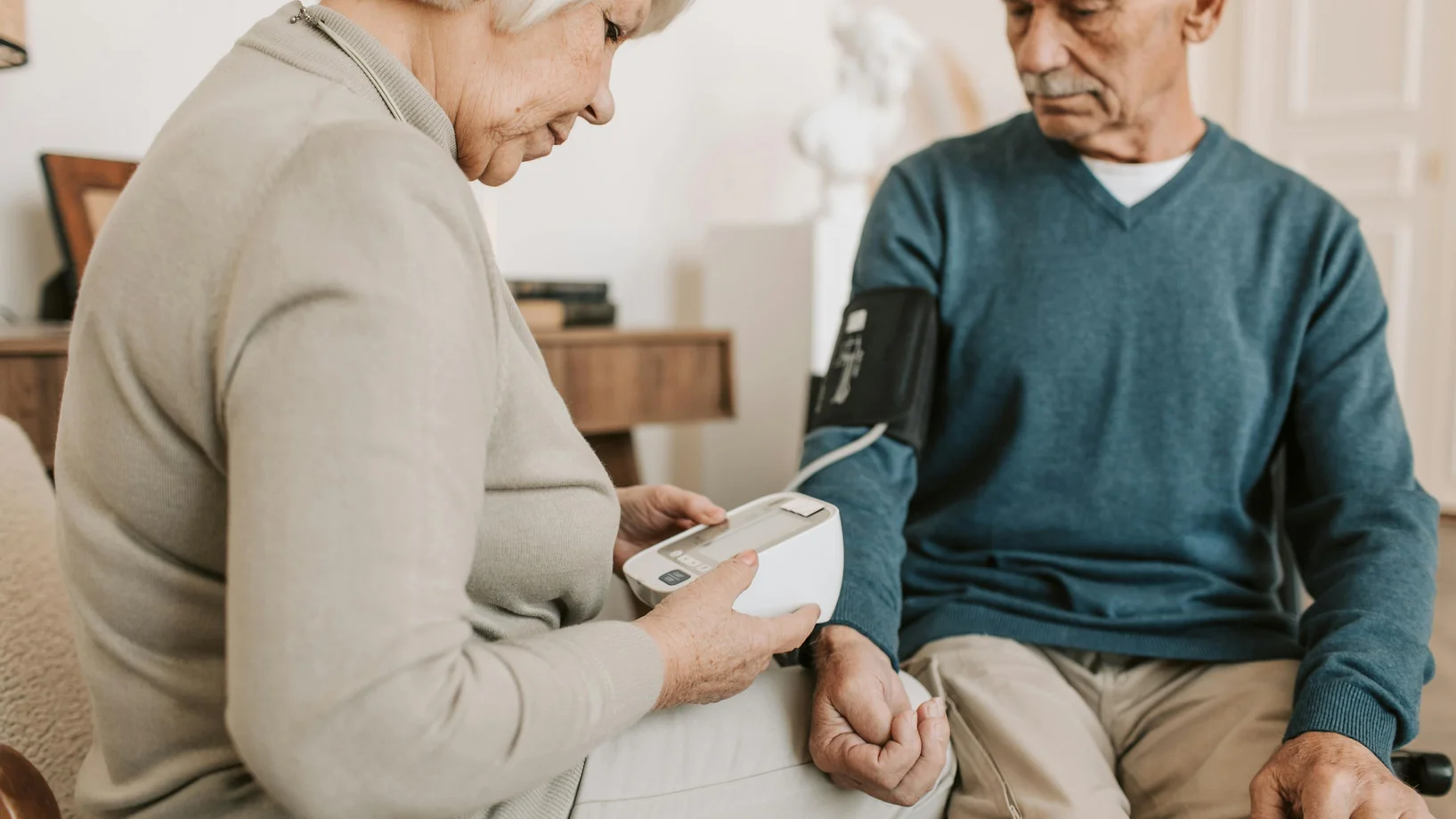 Senior couple at home using a sphygmomanometer to monitor blood pressure, promoting elderly health care.