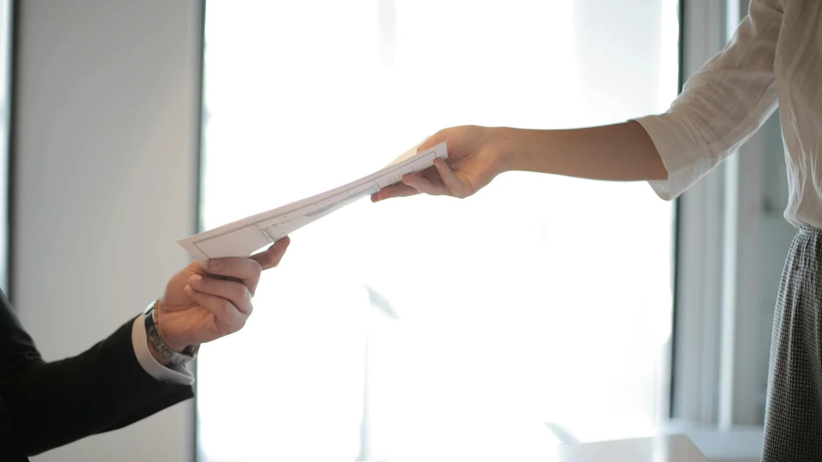 Close-up of hands exchanging documents in a business setting indoors.