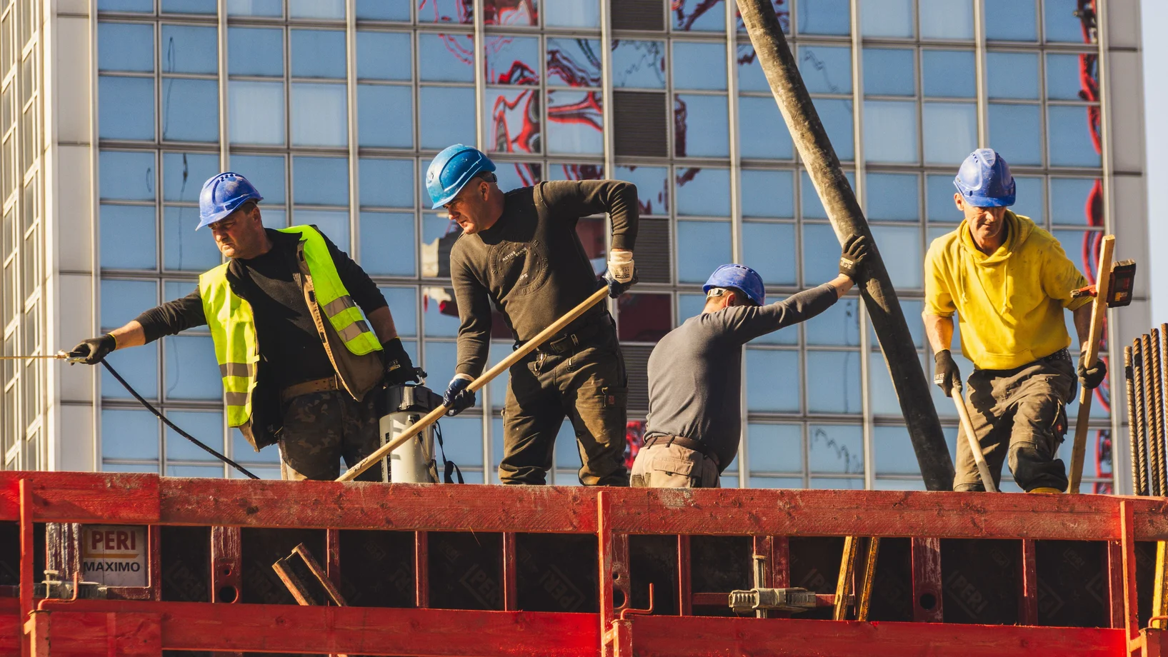 A group of construction workers in safety gear actively working on a high-rise building site.