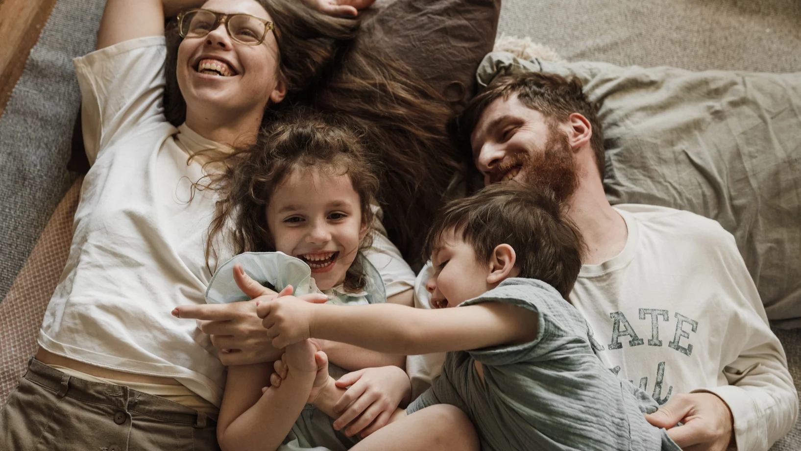 A joyful family bonding moment with children and parents lying together on a cozy bed.