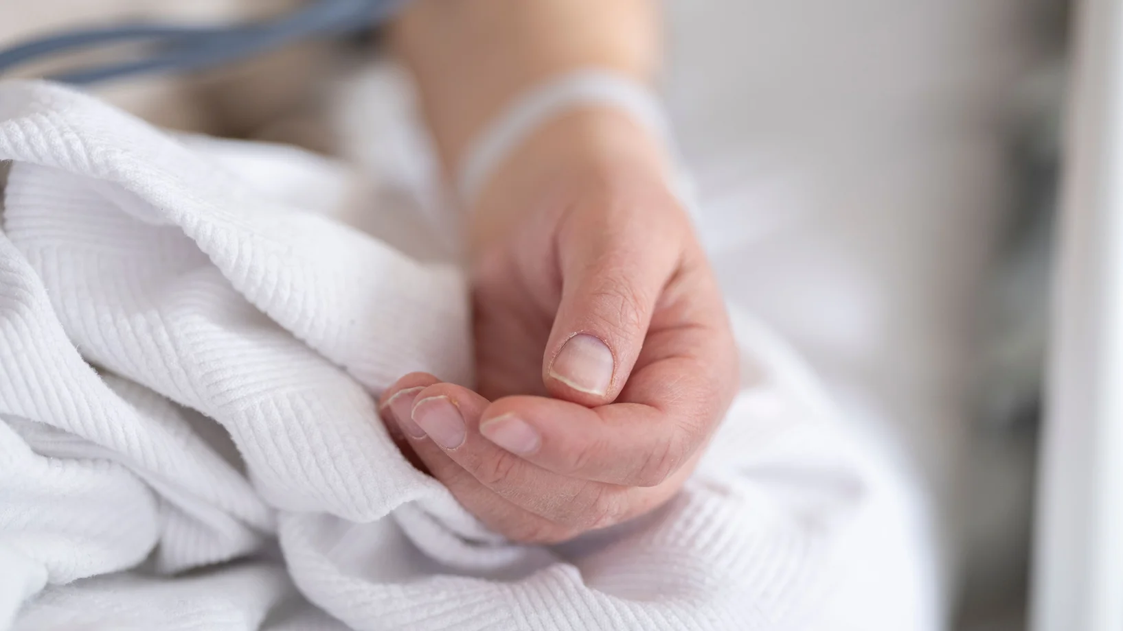 Detailed image of an adult patient's hand resting on a hospital bed with IV line, symbolizing healthcare and recovery.