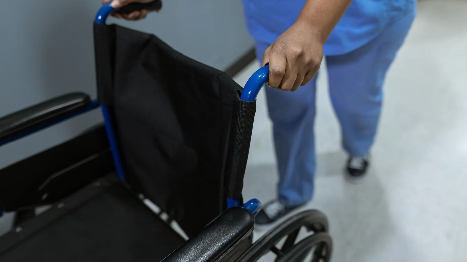 Close-up of a medical worker in scrubs pushing a wheelchair in a hospital setting.